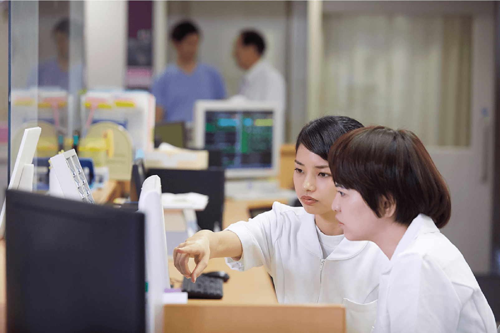 スタッフ2名が病院のナースステーションでパソコンの画面を見ながら真剣に話し合っている様子